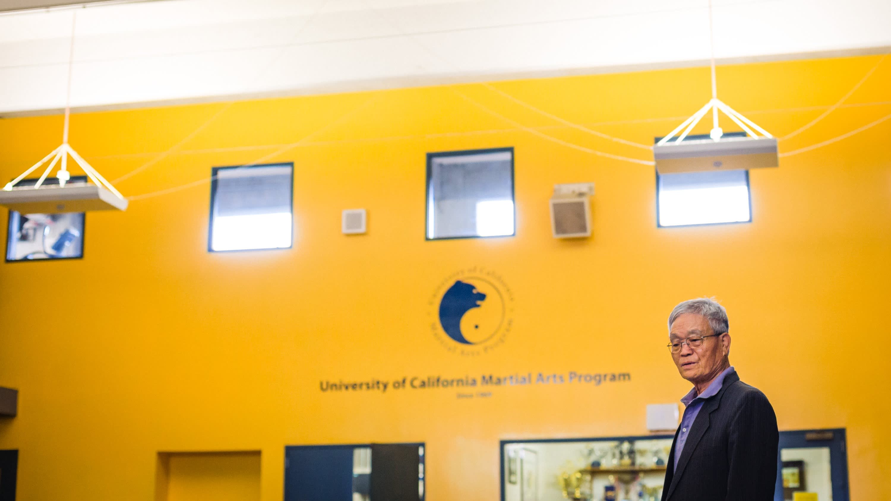 An older Korean gentleman in a suit jacket and button-down shirt against a bright yellow wall. Dr. Min in 2016 in 145 RSF, addressing students.