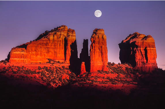 A red rock formation with the moon in the background with Cathedral Rock in the background
Description automatically generated