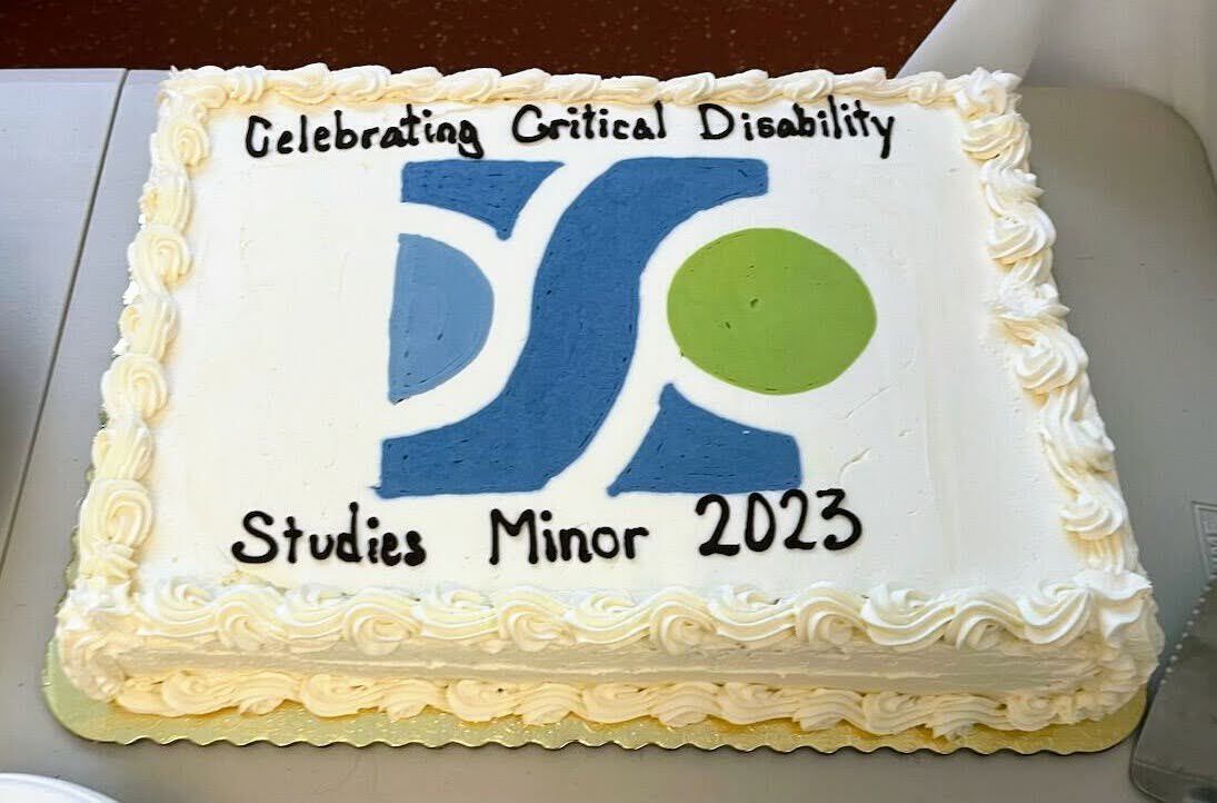 A white rectangular celebration cake that reads, "Celebrating Critical Disability Studies Minor 2023" and has the ICDS logo in blue, light blue, and spring green in the center.