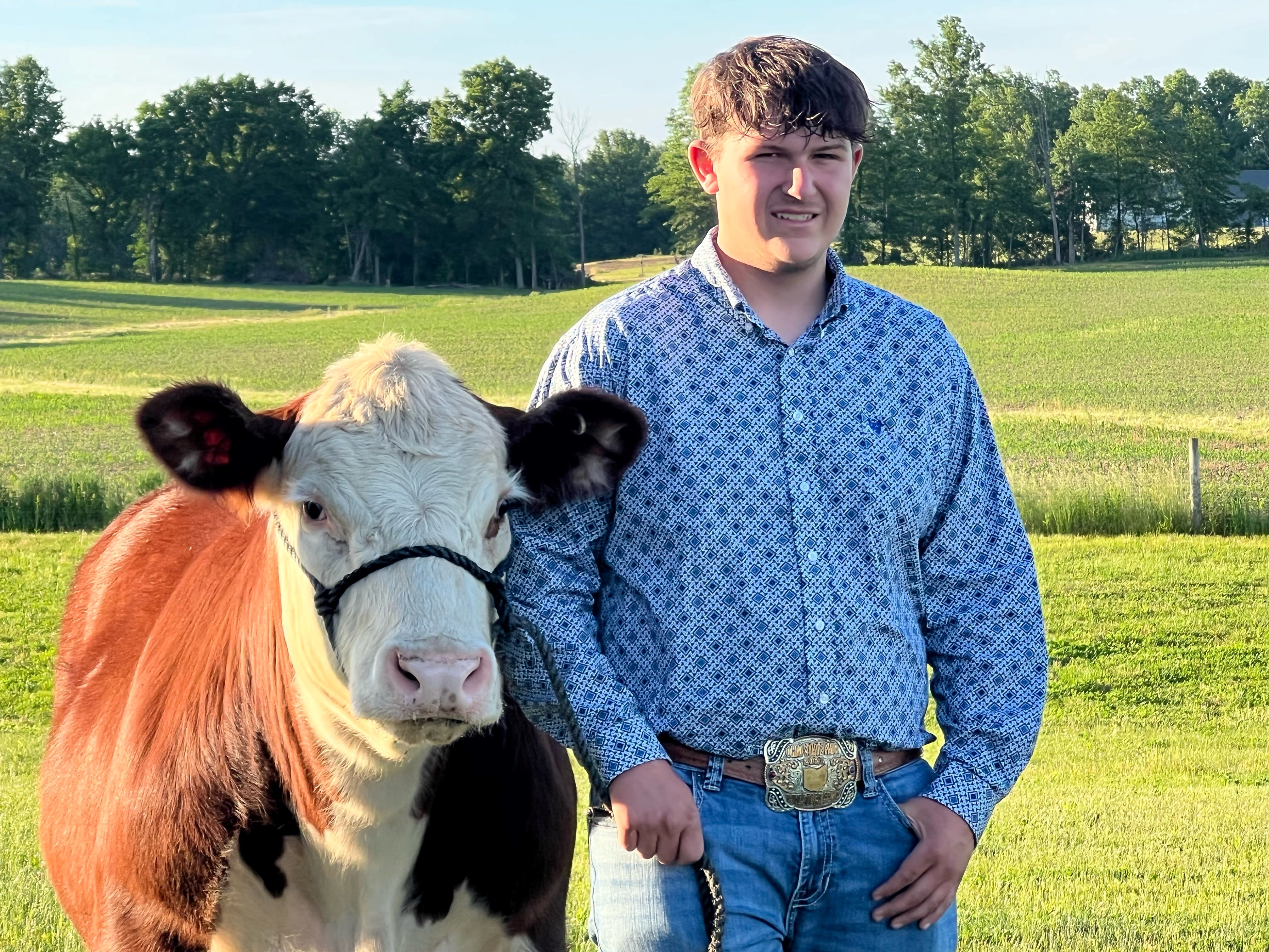 A boy standing outside in showing attire standing beside his steer. He leans gently into the shoulder of the cow