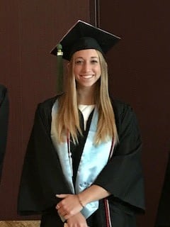 Hannah Ross in her graduation cap and robe. She is posed before a black background