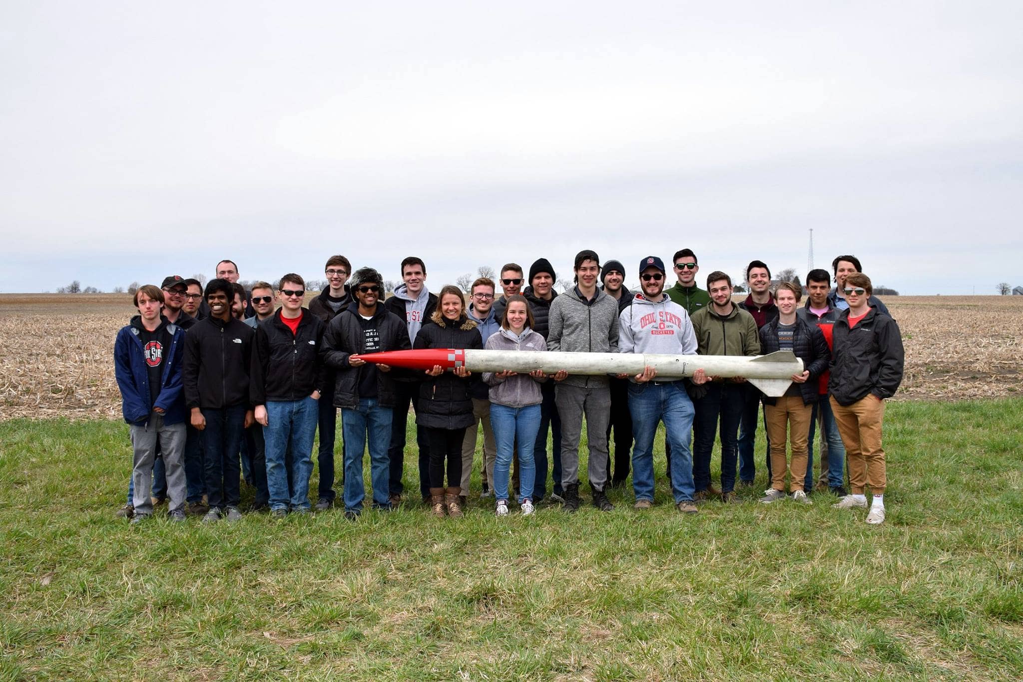 Students holding a model rocket. Behind them is a cornfield