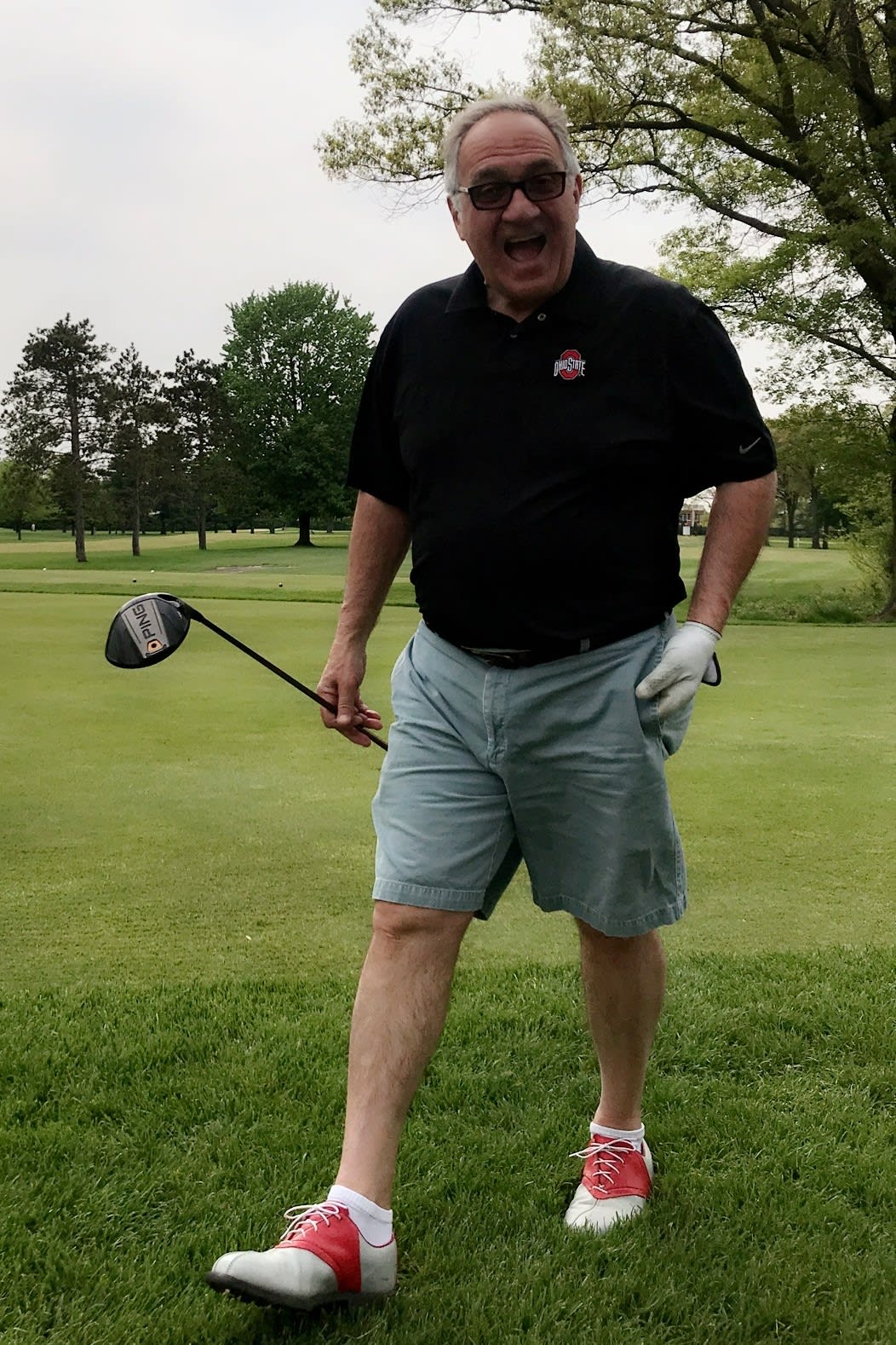 George Kentris smiling widely for a picture. In his nongloved hand, he holds a golfing club