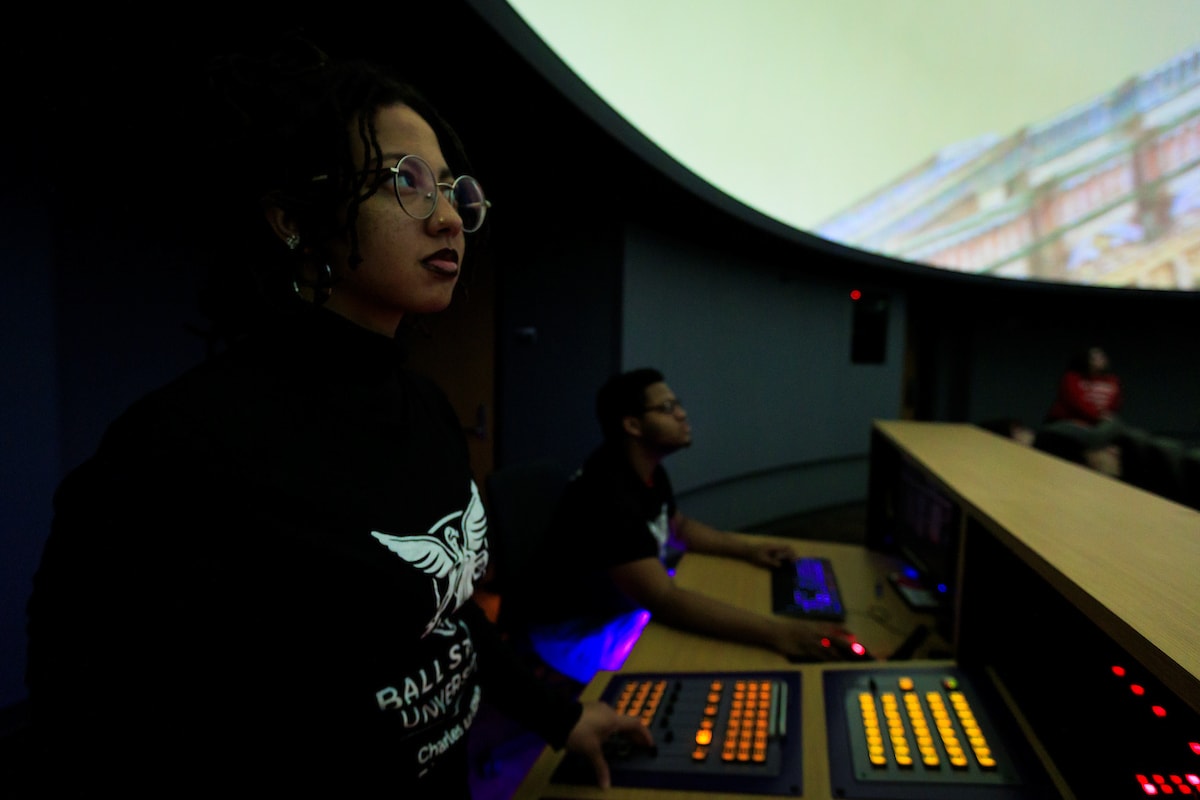 student workers at the control panel of the planetarium, buttons and sliders visible