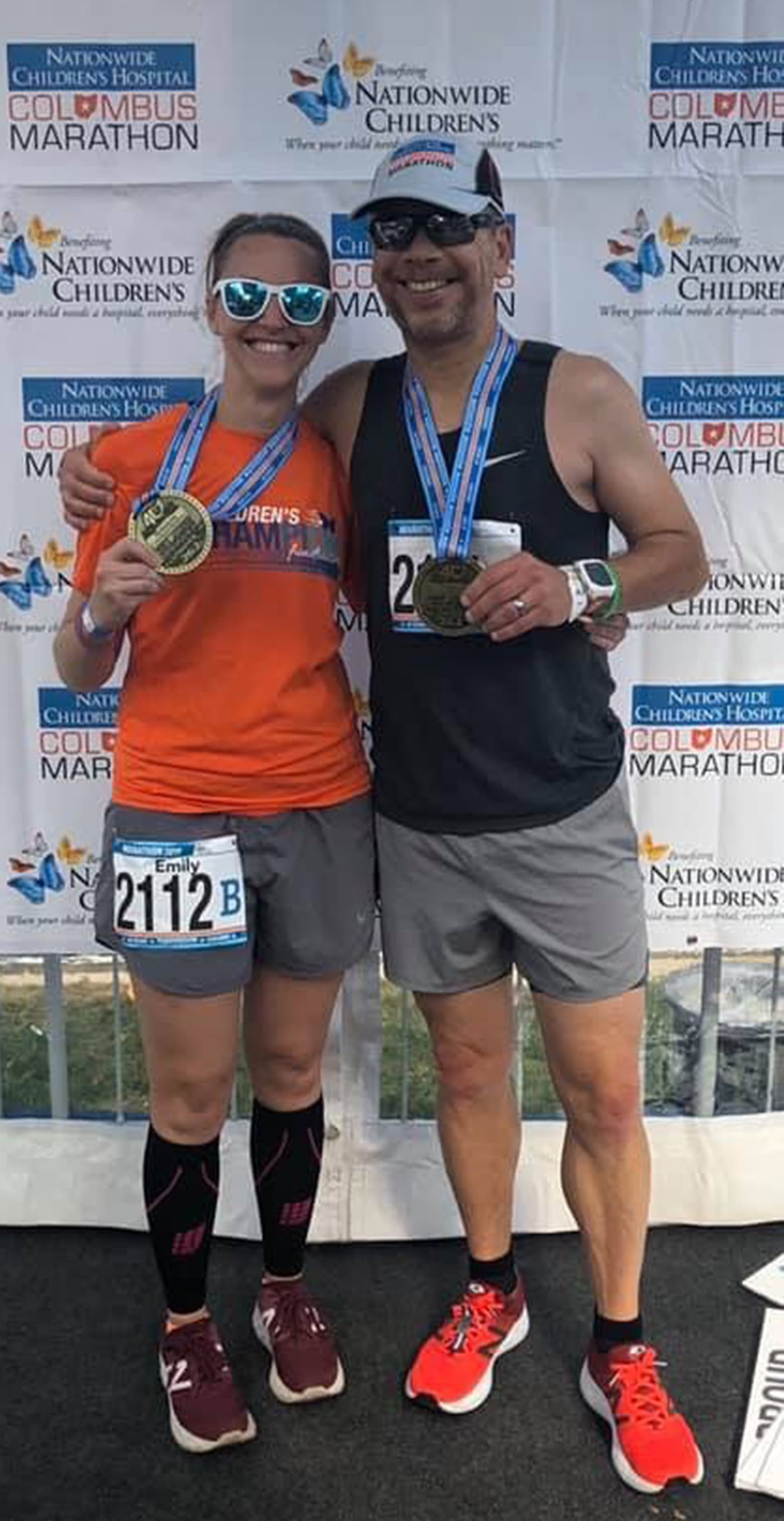 Two runners post-race. They are both wearing and holding their medals