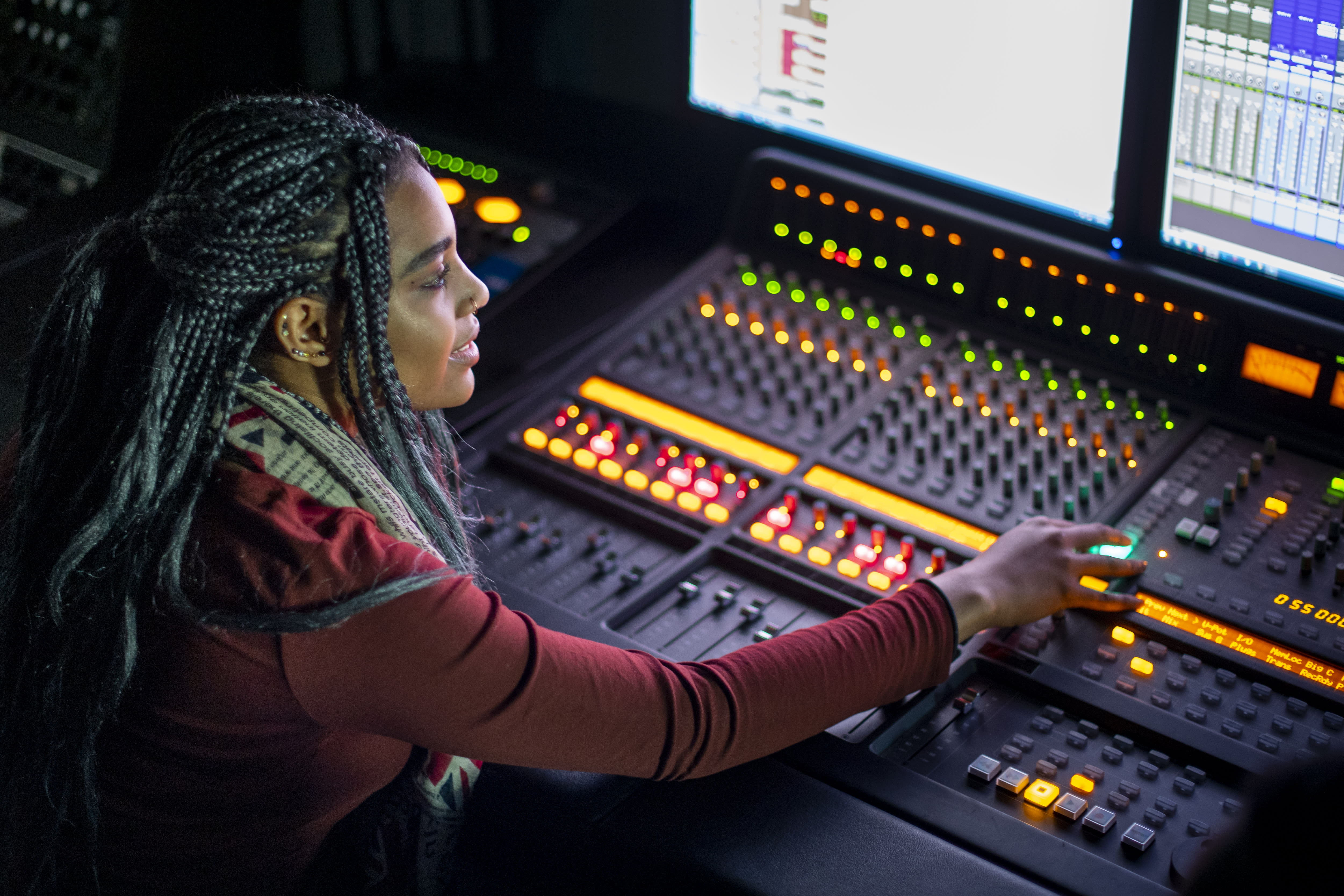 A student sits at a soundboard, adjusting a knob.