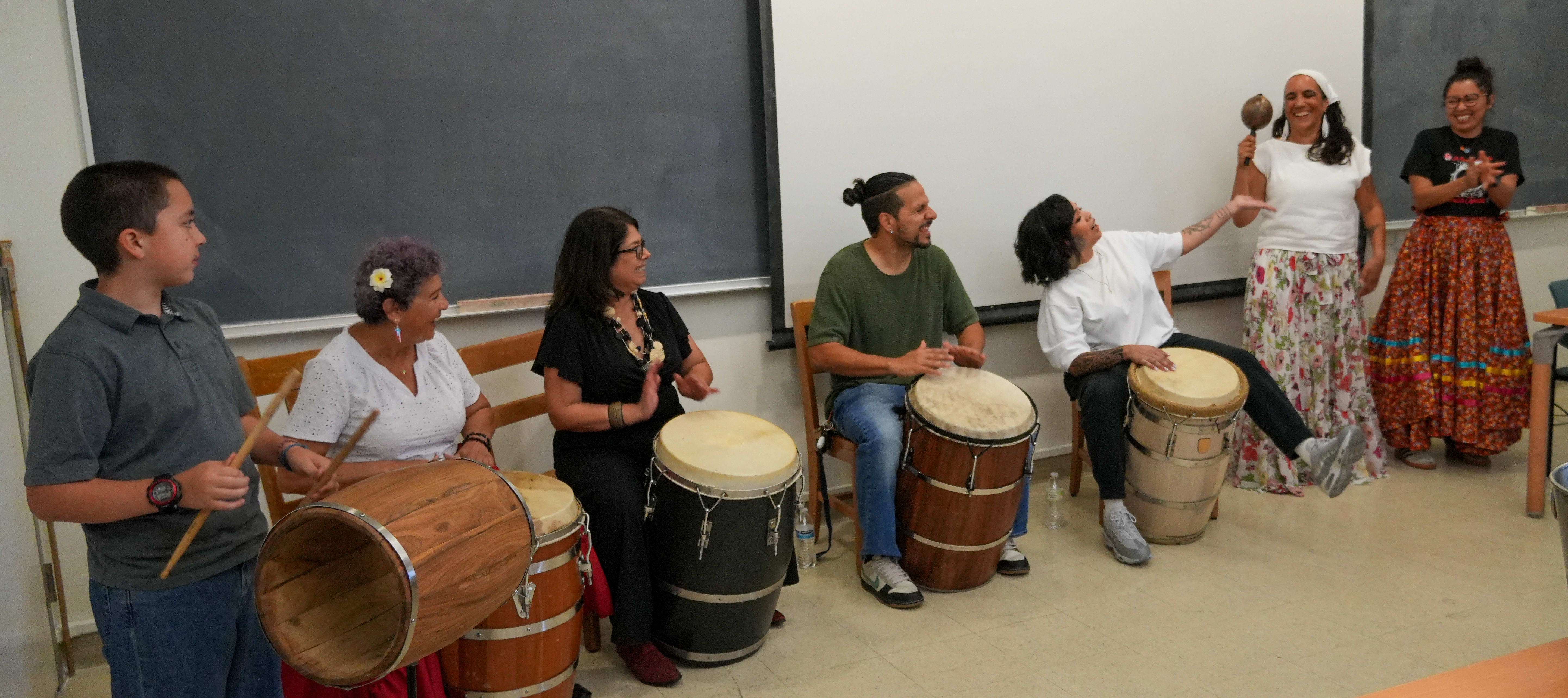 Students and performers play drums at a bomba performance in a classroom