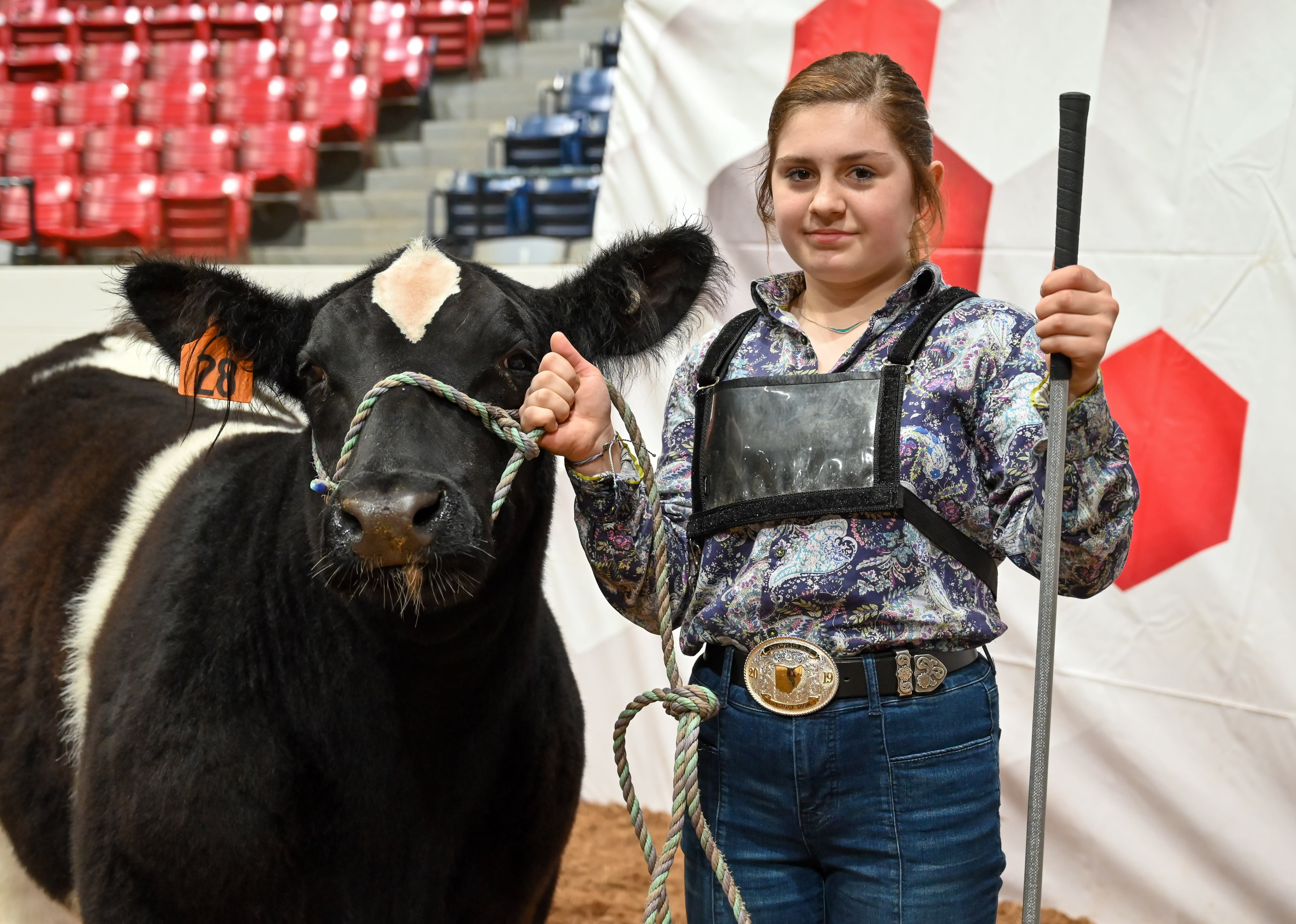 A girl holding the rope of her black and white cow. In the other hand is a guiding stick
