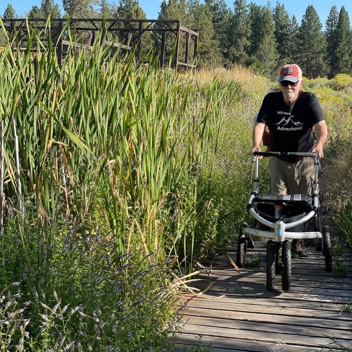 A person pushing a walker on a wooden path

Description automatically generated