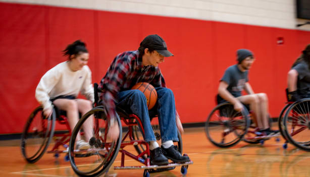 One in-focus student playing wheelchair basketball, with several out of focus teammates and competitors behind them. 