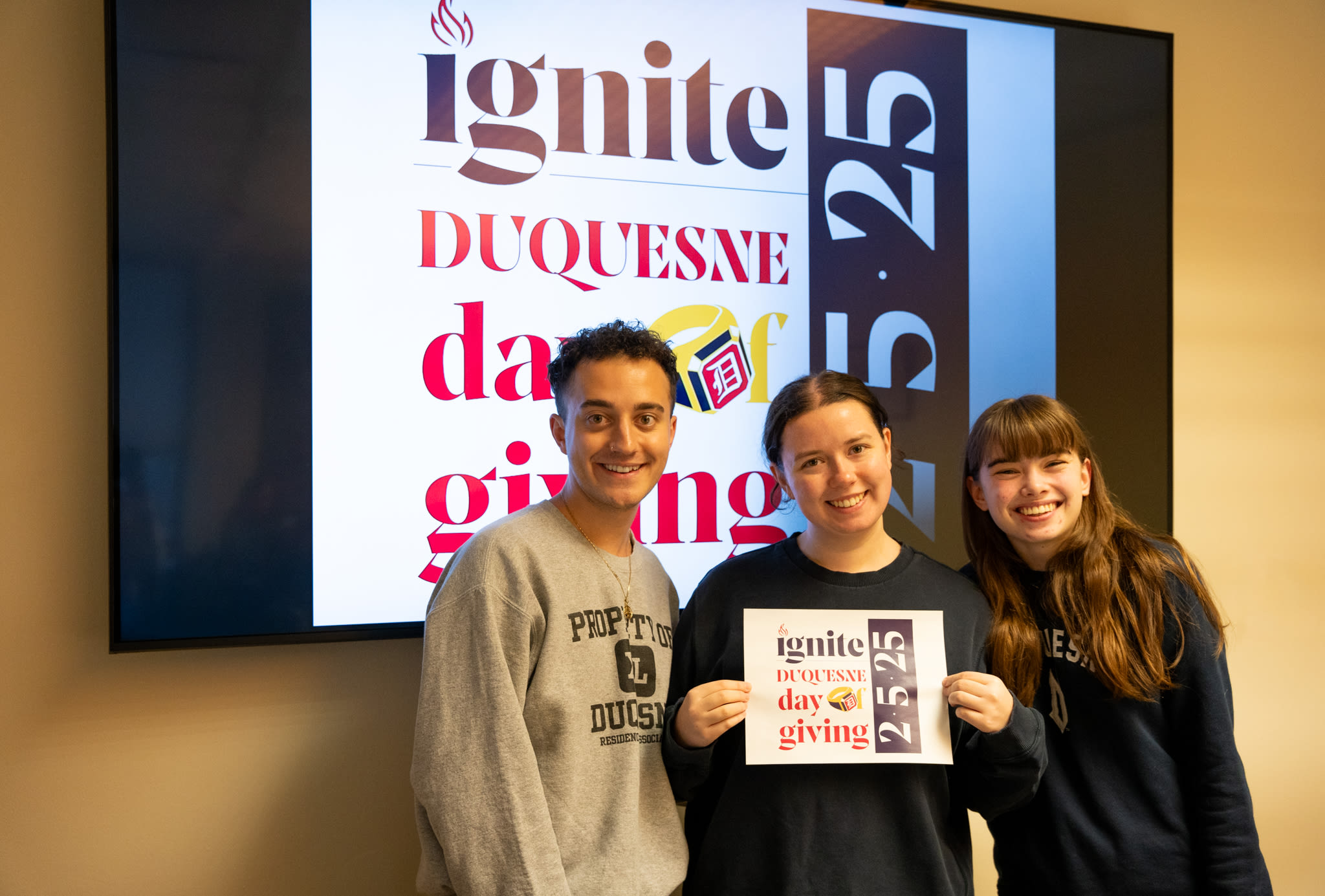 Three Liberal Arts students smiling and holding a Day of Giving sign