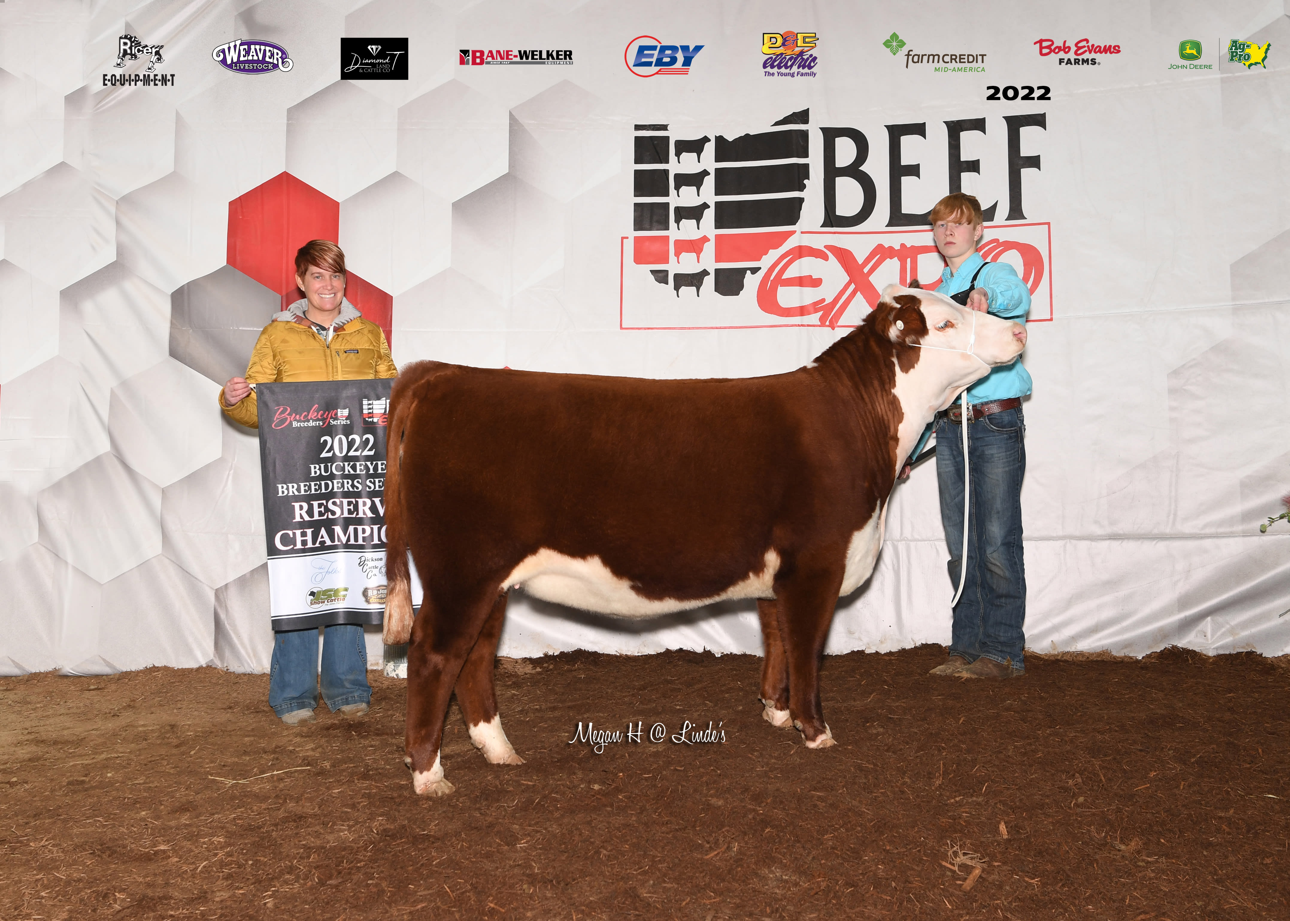 Two individuals stand in front of a Beef Expo backdrop. One handles a brown and white cow while the other holds a banner