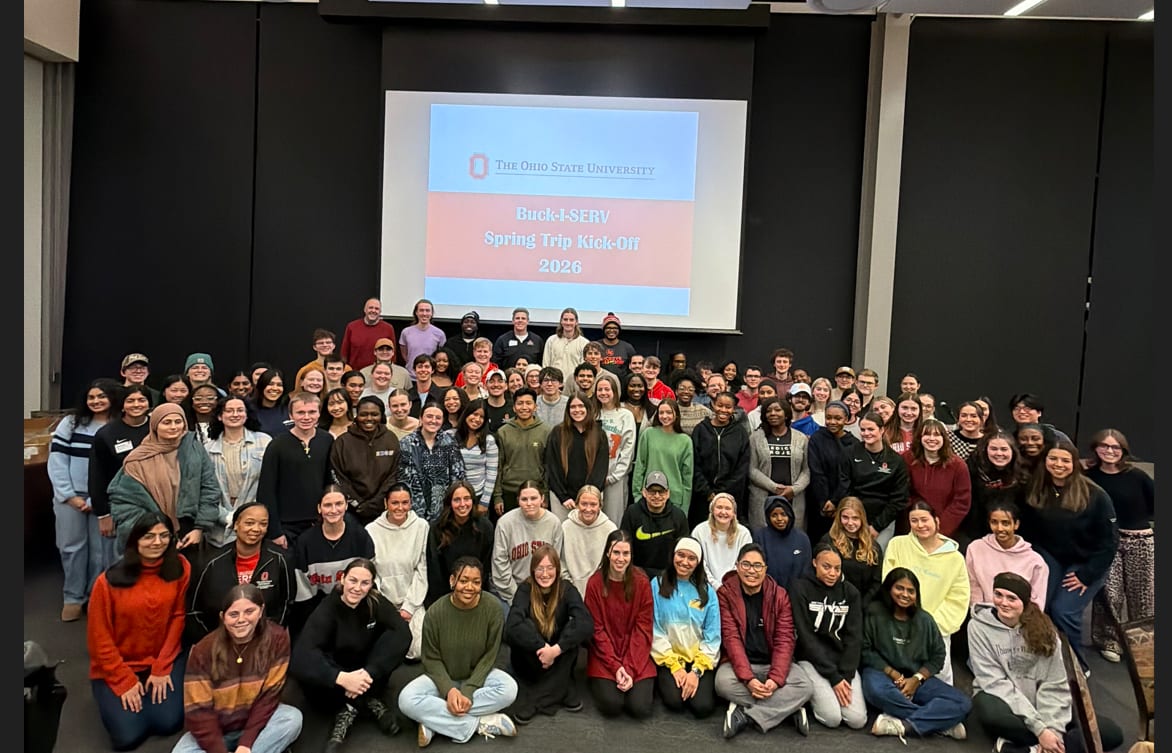 A large group of students posed in front of the projection 'Spring Trip Kick-Off 2024' slideshow 