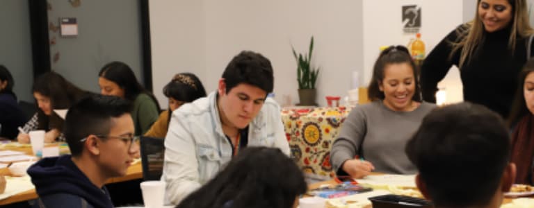 7 students seated around a table doing school work and talking