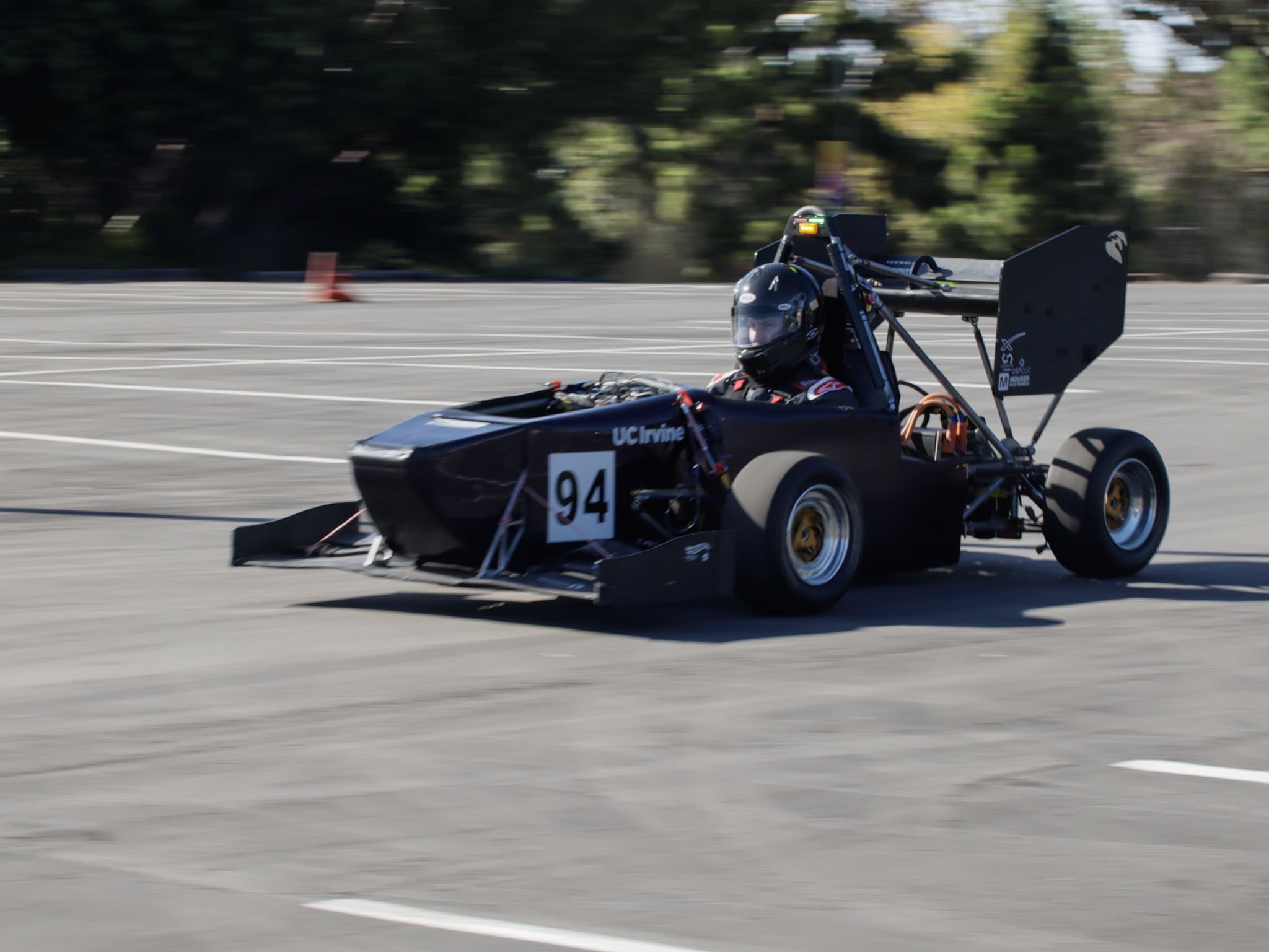 An action shot of the racecar being driven through a parking lot. The number "94" is clearly visible next to a large "UC Irvine" logo.