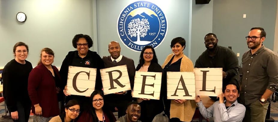 7 people standing in a row. 5 holding signs that speall out C R E A L