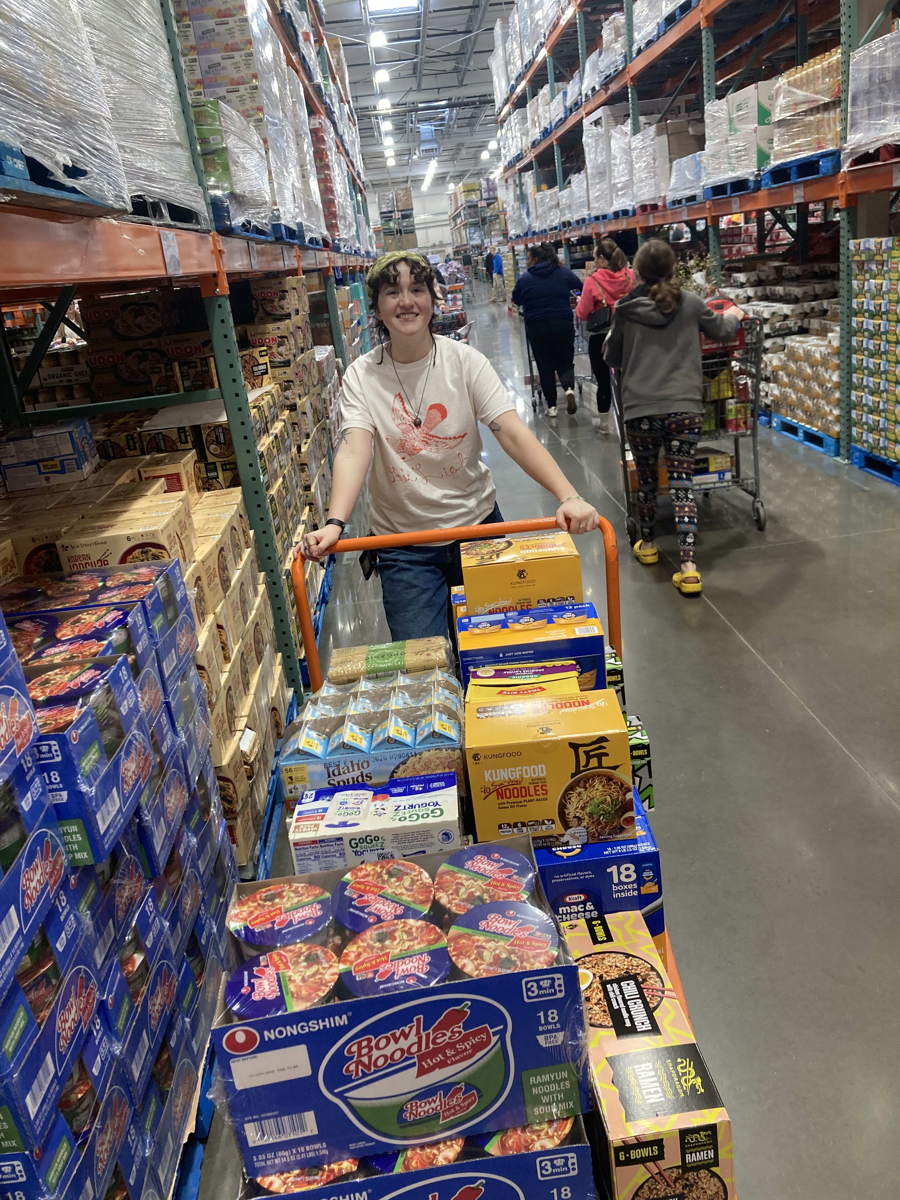 A smiling person pushes a large cart full of groceries in Costco.