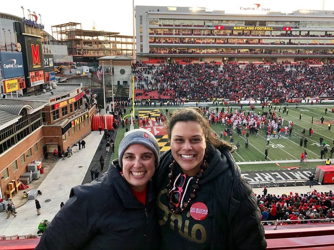 Melissa smiling with her friend, Jenn, in front of the University of Maryland football field. Celebrating the 2018 win against Maryland.