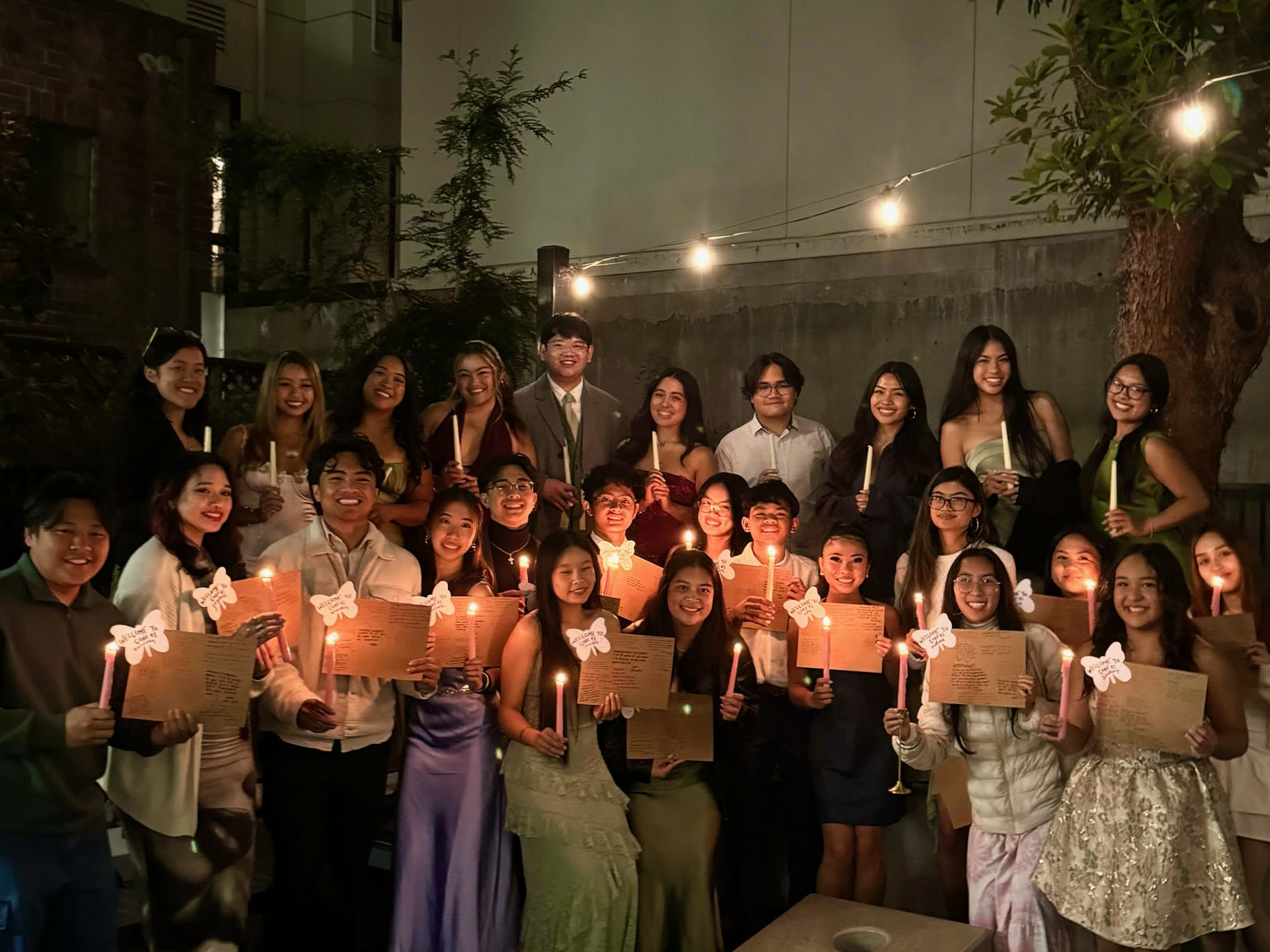 Students in formalwear at night holding candles and signs at the PAHCtillion event.