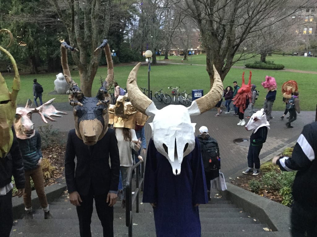 humanoids with startling animal heads and skulls in a park setting. Onlookers gape.