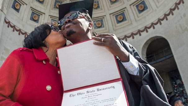 Women kissing man on the cheek while holding his diploma