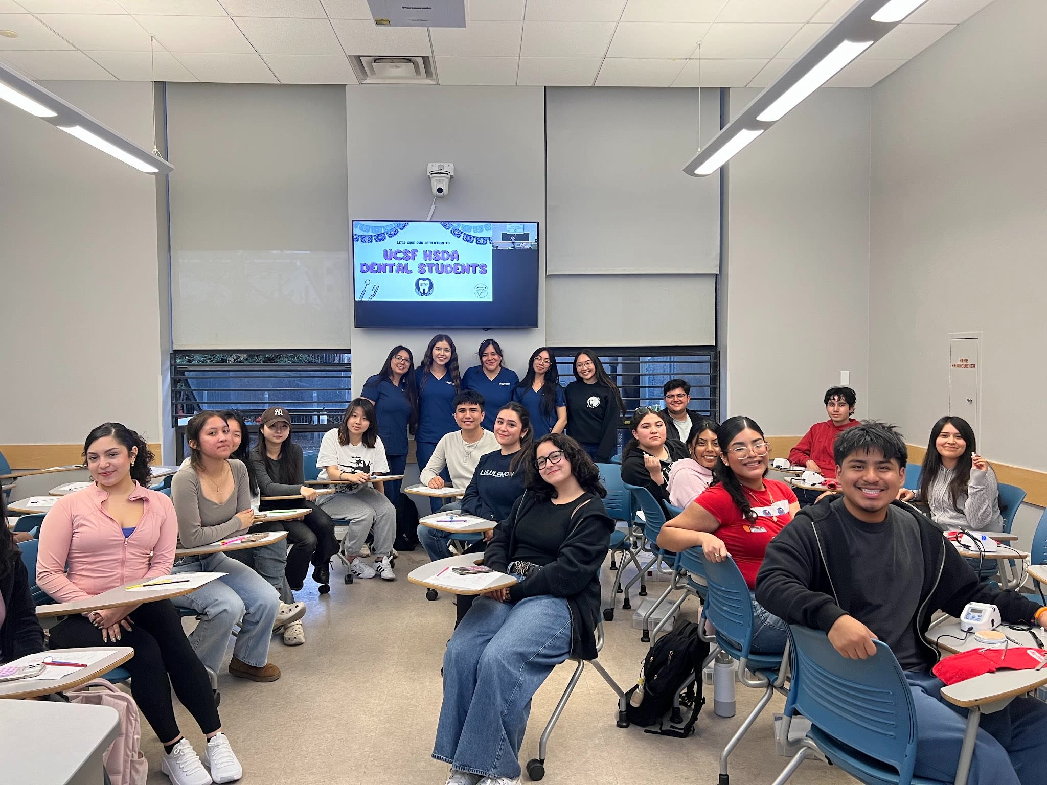 Group of LPDS students sitting in desks in a classroom, smiling at the camera.