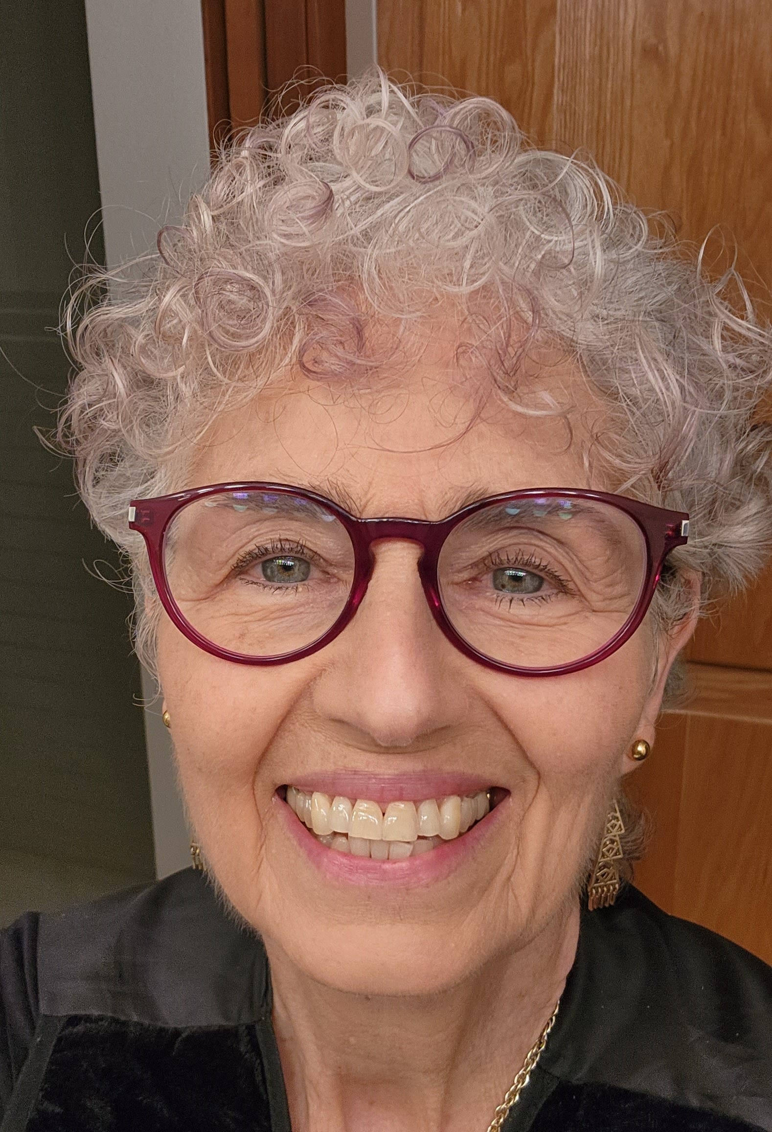 Millie Johnson, a white woman with curly white hair and large cat-eye glasses, smiles at the camera