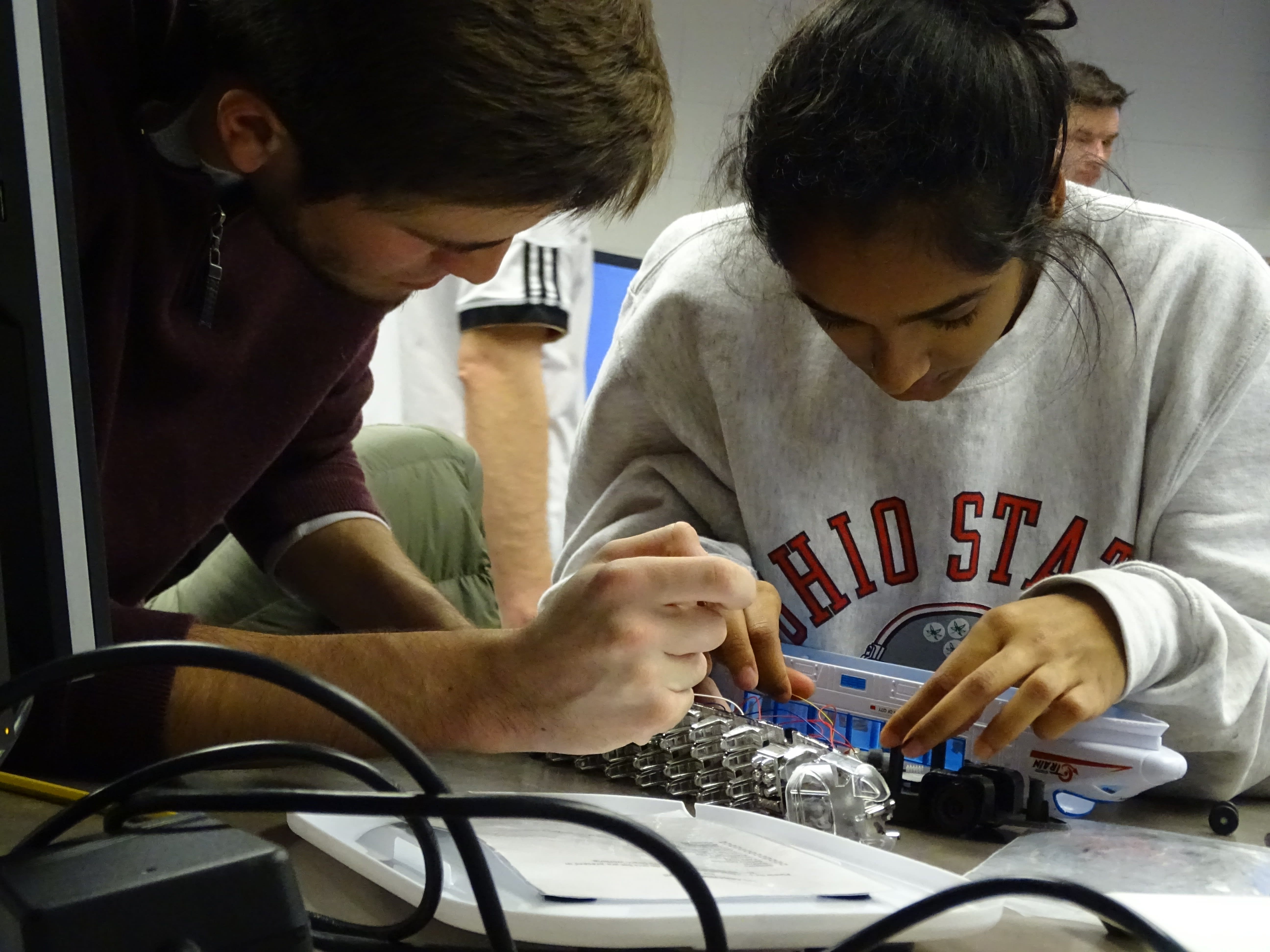 Two individuals work with a toy and its wires