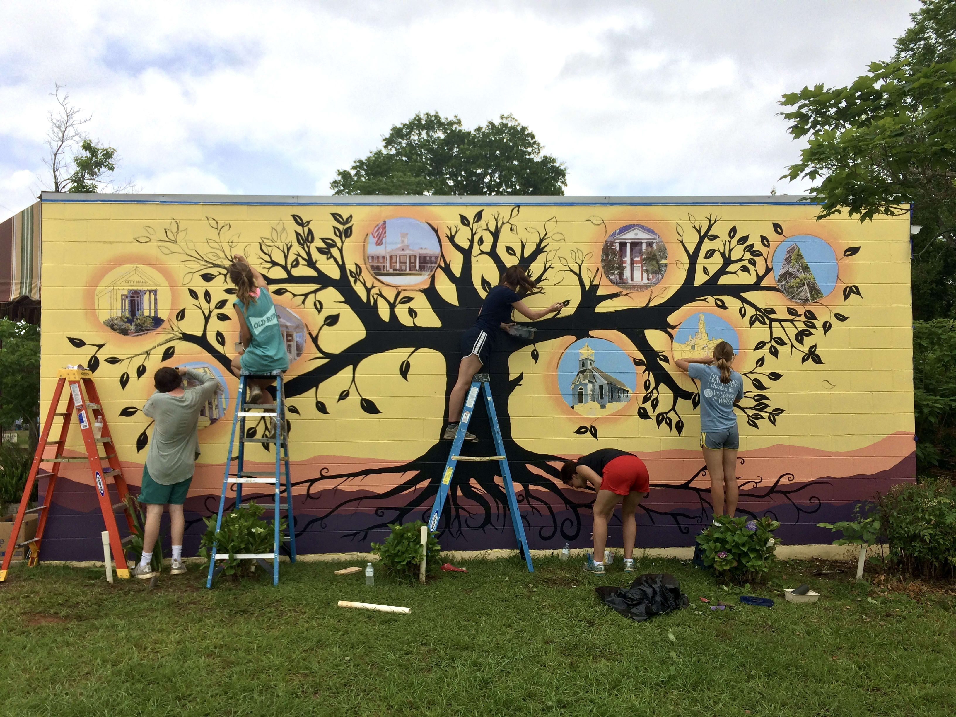 A group of people painting a tree on a wall

Description automatically generated