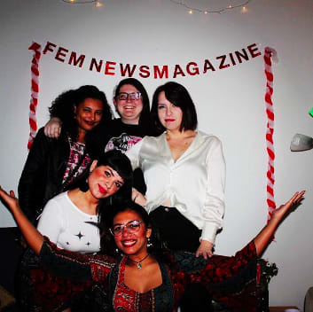 FEM members gathered in front of a red sign that says FEM Newsmagazine