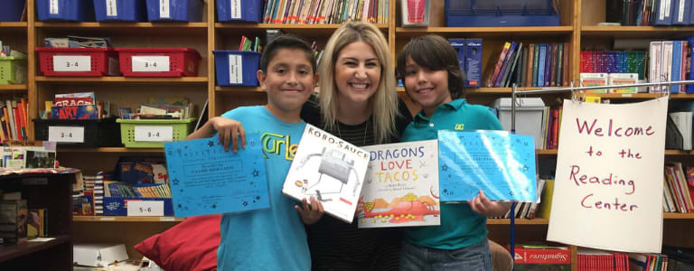 women crouched down with two children either side of her smiling and holding books