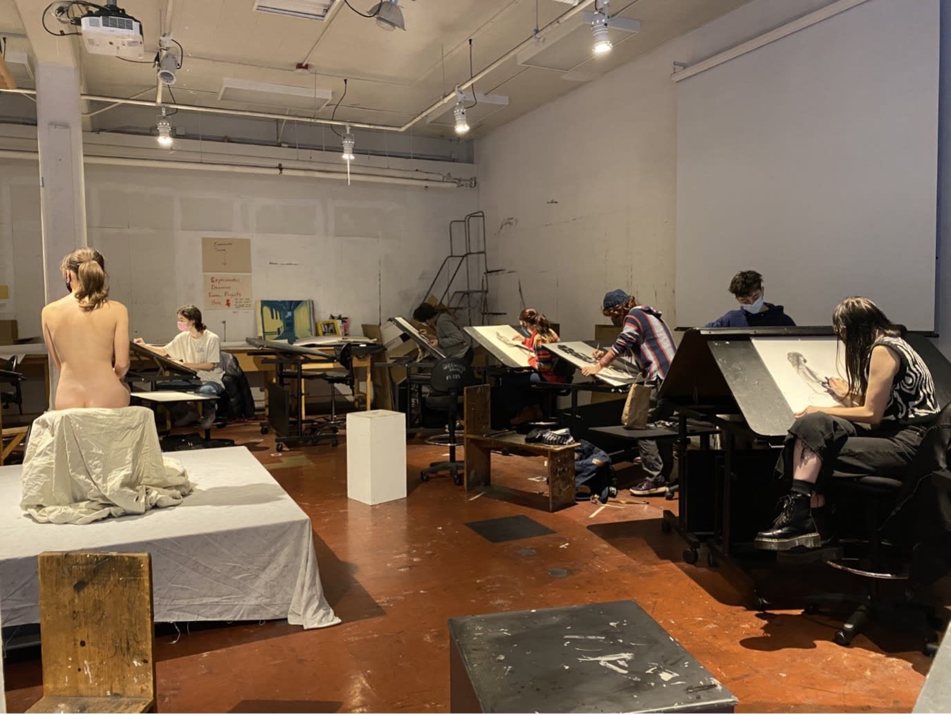 students in a studio draw a live model posing on a chair