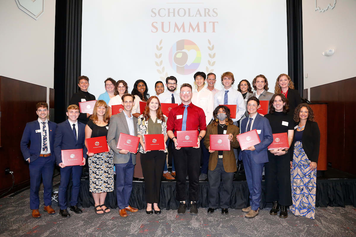 Students standing before a projected 'Scholars Summit' screen, holding their diplomas