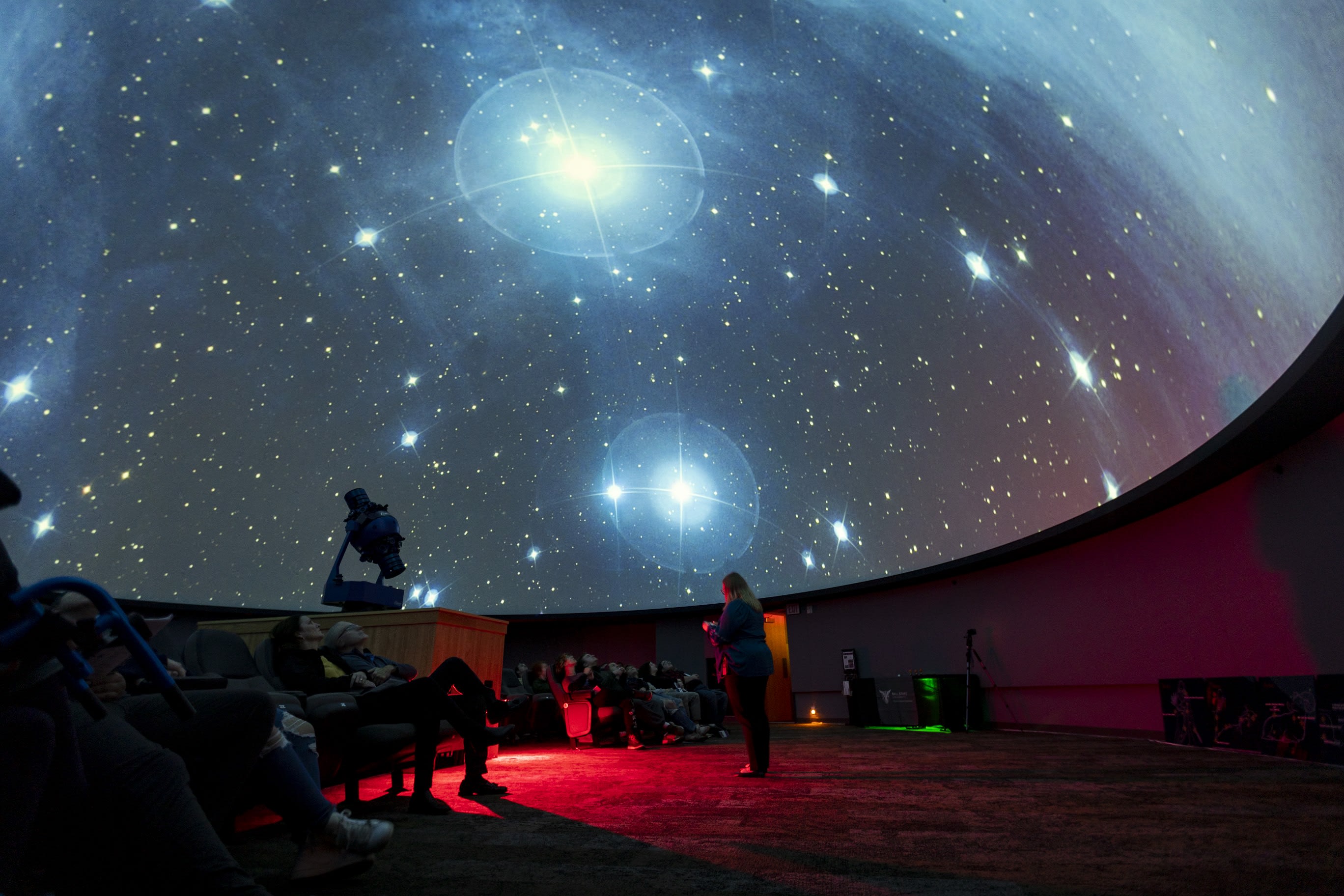 student worker presenting in front of a full planetarium with the pleiades star cluster overhead on the dome