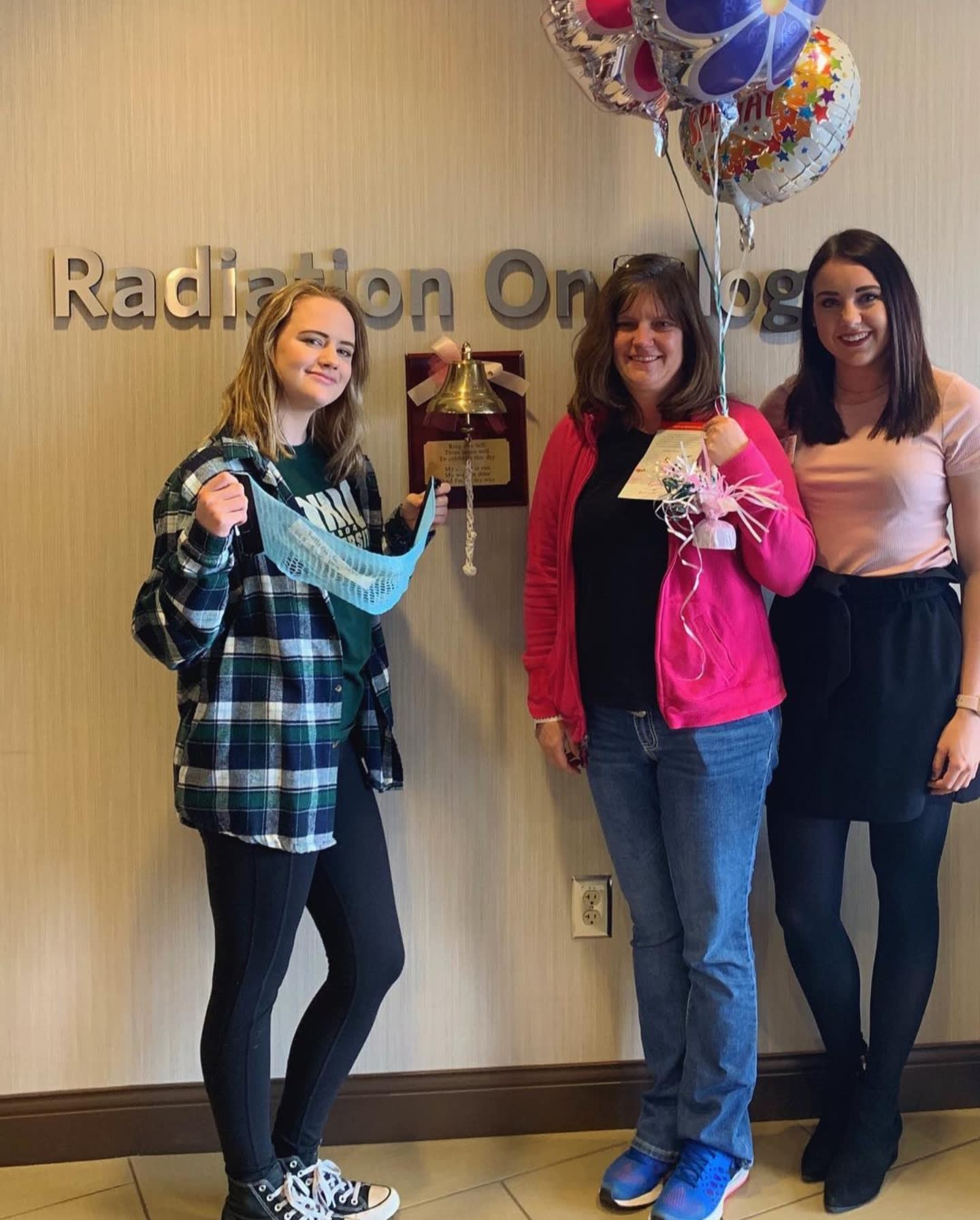 Three women stand around a Beating Cancer bell