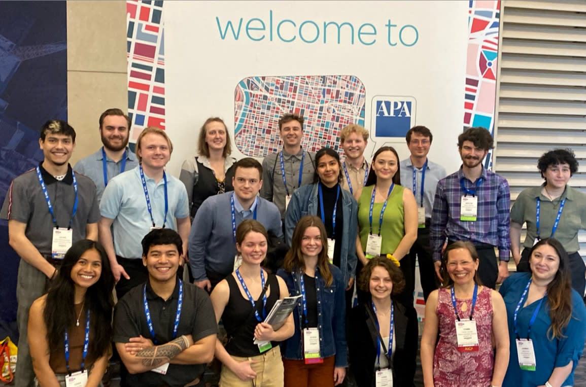A large group of people pose in front of the APA conference welcome sign.