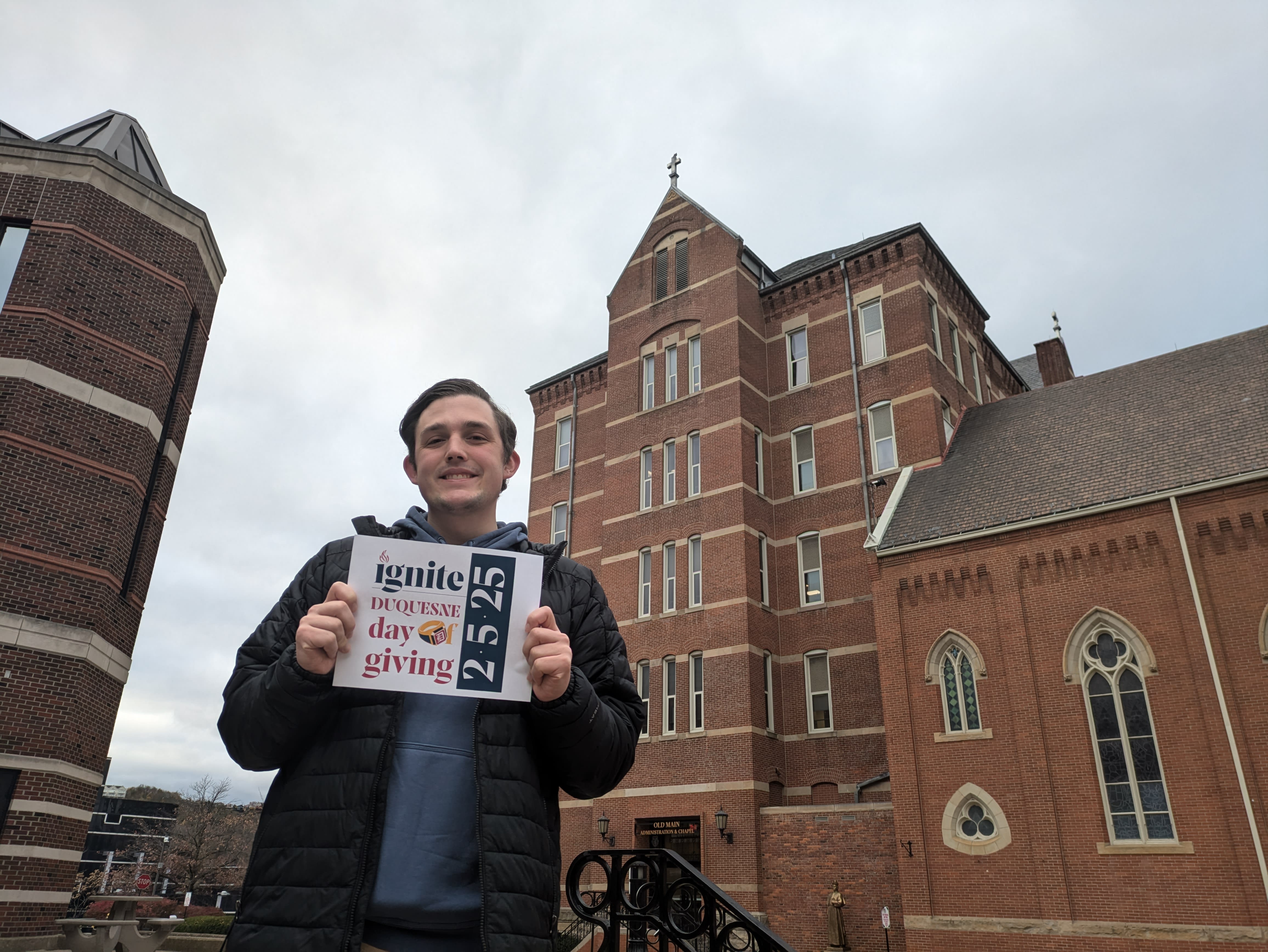 Student standing in front of Old Main holding a Day of Giving sign