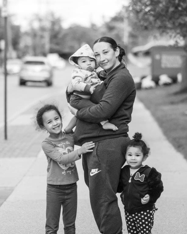 With a baby in her arms, a mother stands with two more children at either hip