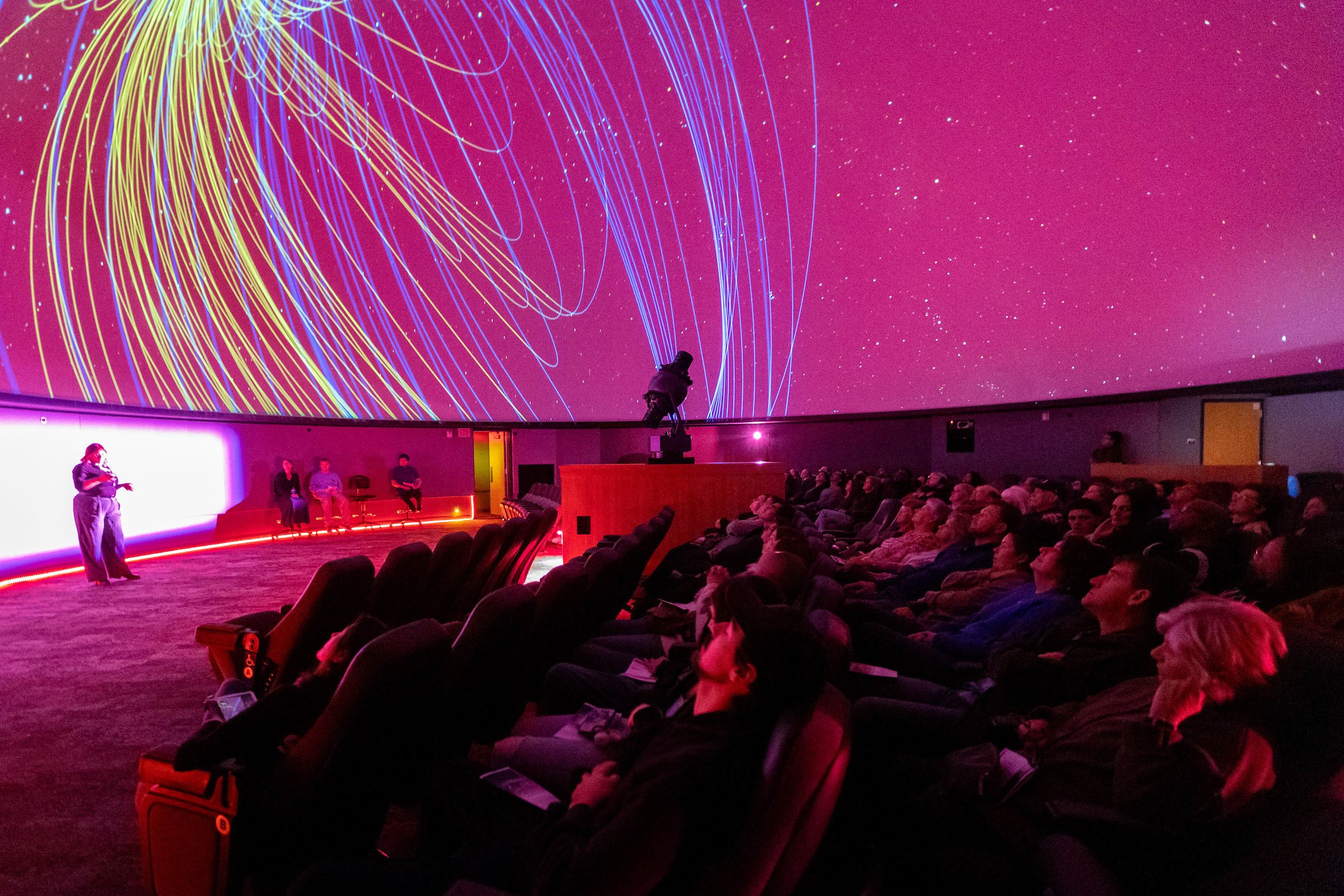 student worker presenting in front of a full planetarium with the Earth's magnetosphere overhead on the dome