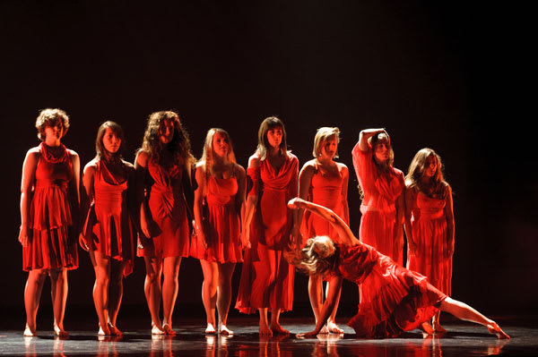 seven dancers in red light, with one dancer propped on the floor at angle in front