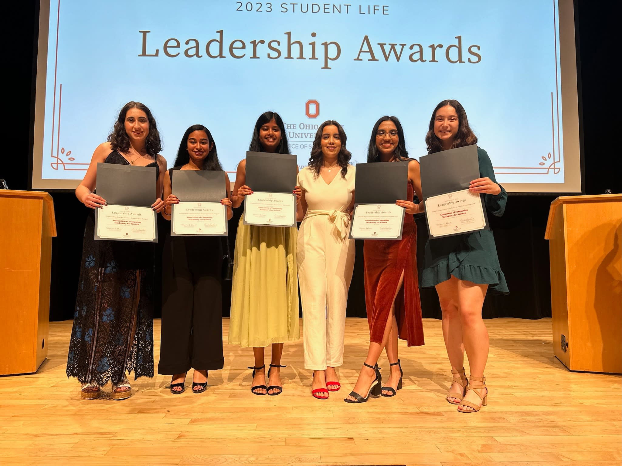  Six individuals standing on a stage holding a leadership award