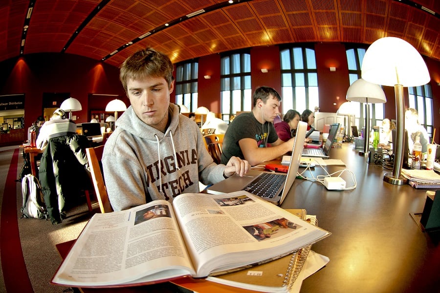 Students studying in Torgerson Bridge at Virginia Tech with books and a computer.