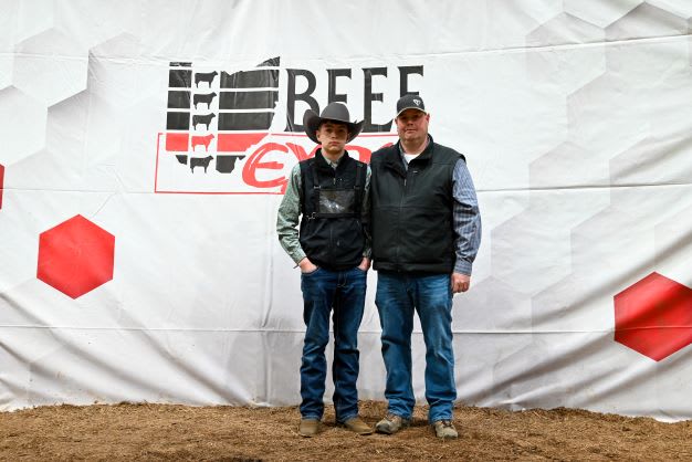 A boy stands next to a man before the Beef Expo backdrop 