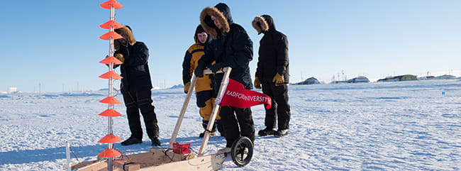 Students dressed in winter clothing pushing self-made equipment across the ice with a Radford University flag