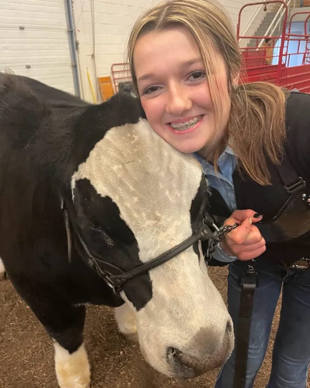A girl presses the side of her face to a steer's head, smiling towards the camera