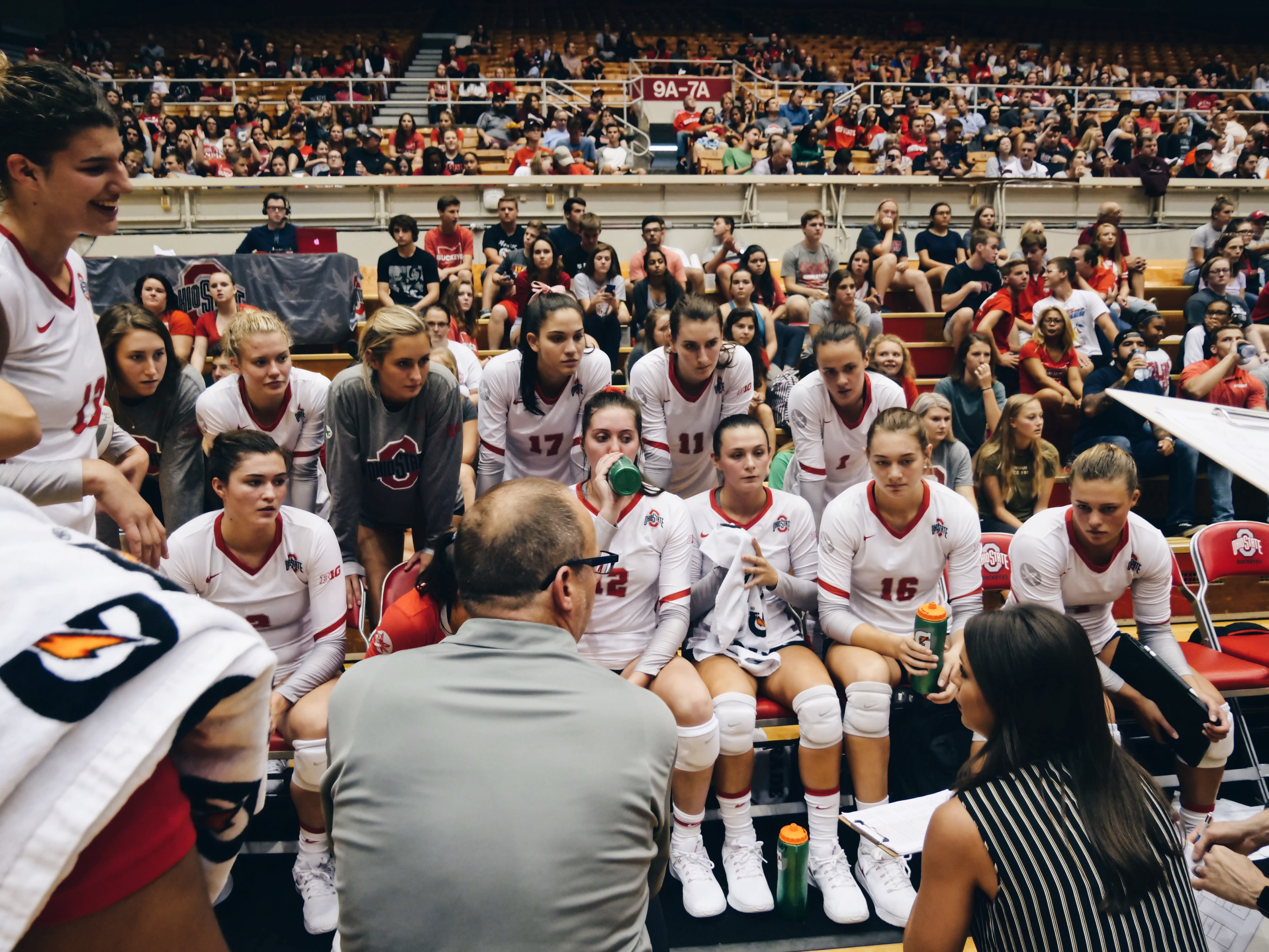 The women's volleyball team intently listening to their coaches while taking a break