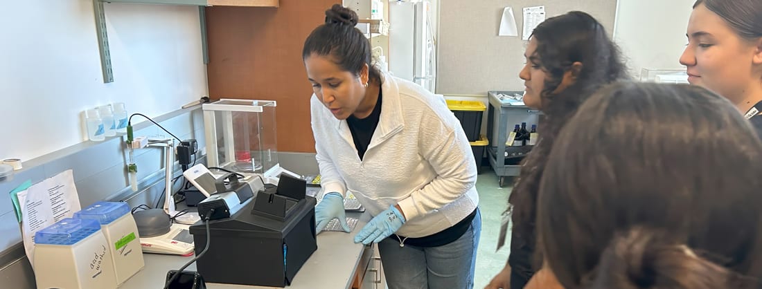 Laura Martinez Robles showing students with the Na Pua Noeau program the results of E. coli samples that tested positive. . E. coli bacteria produce a fluorescent signal under a UV light. The students collected, processed, and incubated pond water samples for E. coli. 
