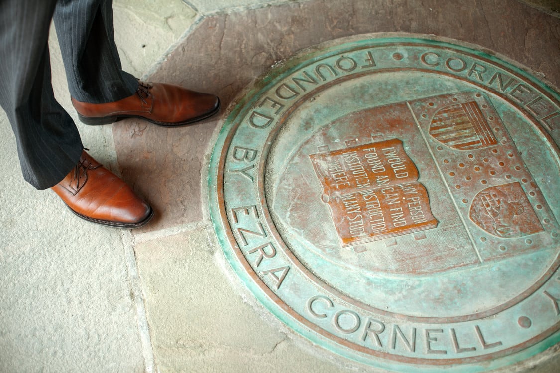 Student in professional attire next to Cornell shield