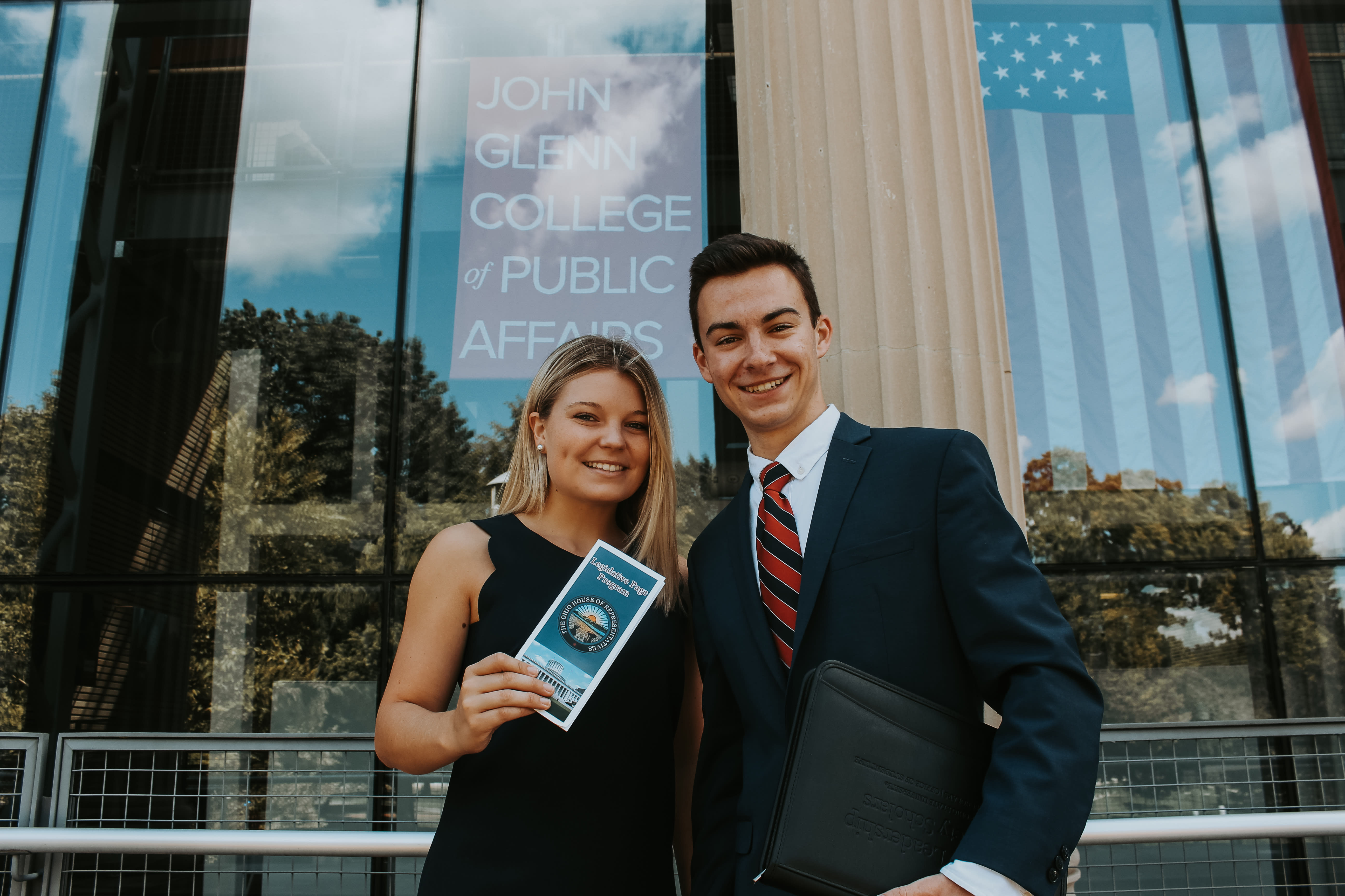 Two members stand before the college of Public Affairs building dressed in business attire