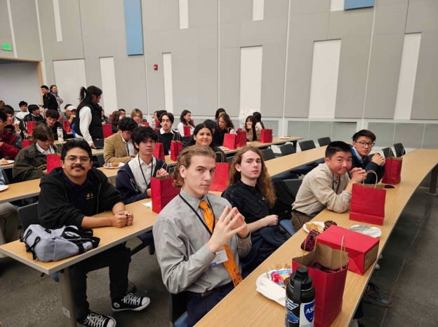 Seven member of the UC Irvine ITE team sit in the front rows of a lecture hall waiting for a presentation to begin with many other students in rows behind them.